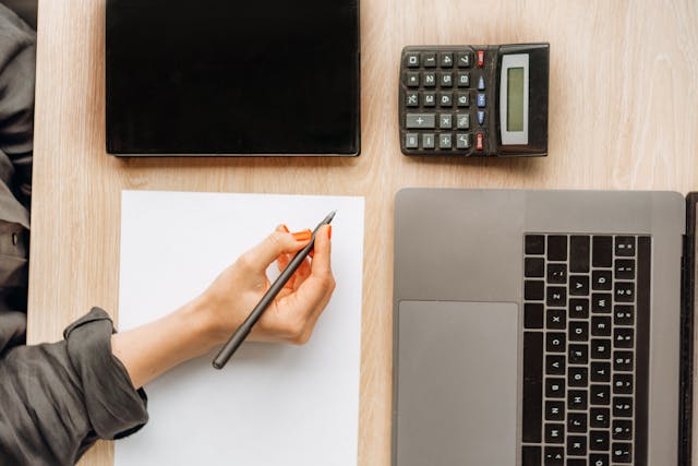 a computer and calcualtor in front of someone writing something